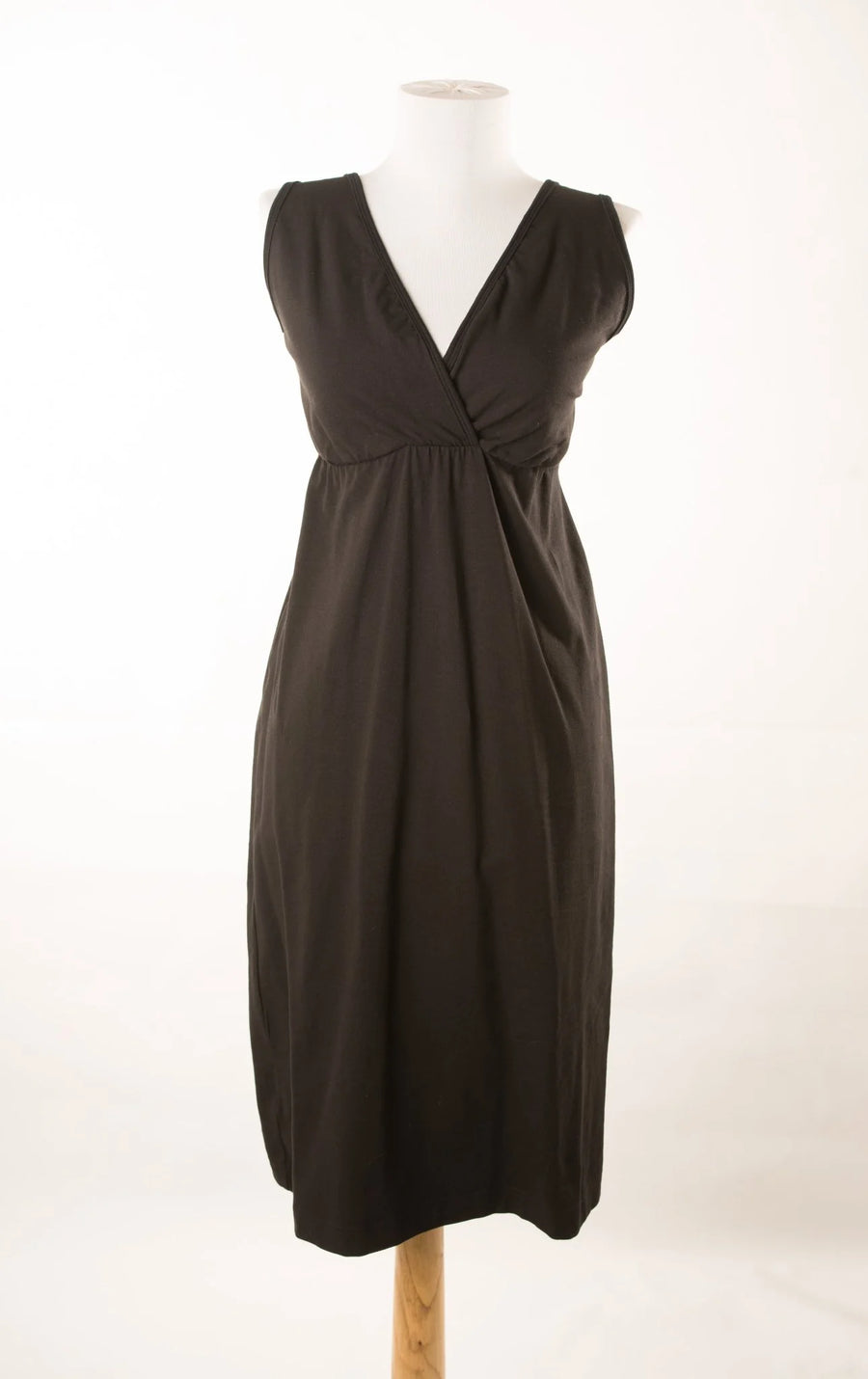 Pregnant woman wearing the black Aimee gown beside a window