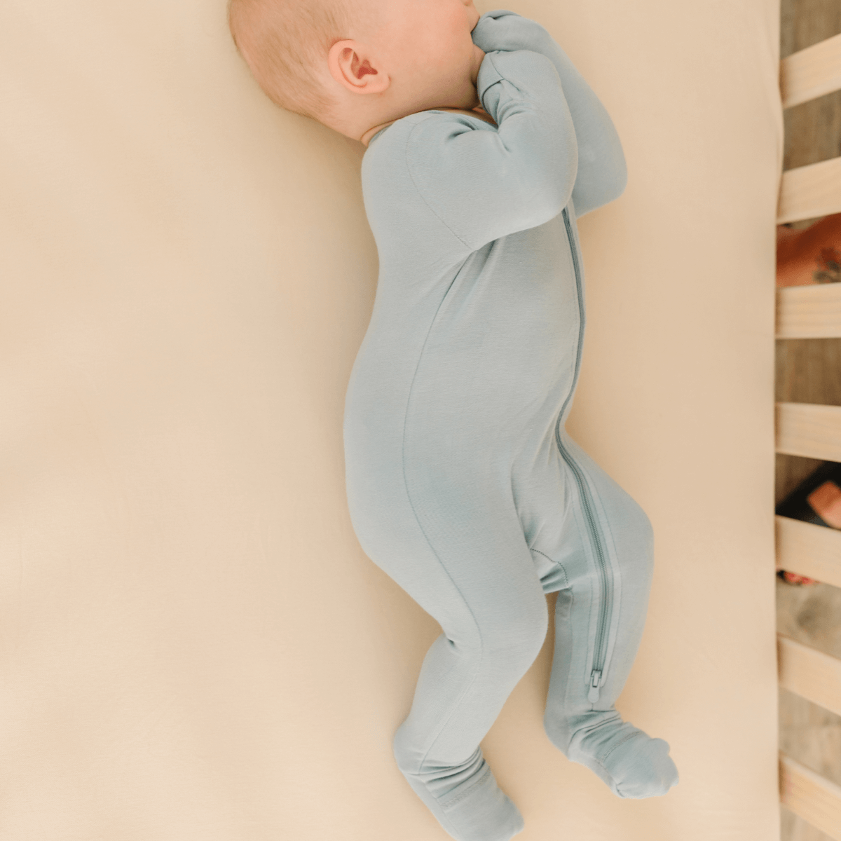 Baby in soft bamboo pajamas with DreamCuffs® from Dreamland Baby, lying peacefully on a cozy blanket.