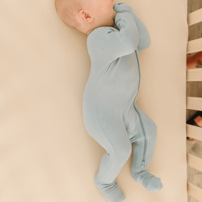 Baby in soft bamboo pajamas with DreamCuffs® from Dreamland Baby, lying peacefully on a cozy blanket.