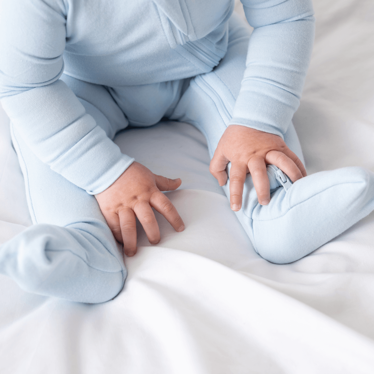 Baby in soft bamboo pajamas with DreamCuffs® from Dreamland Baby, lying peacefully on a white blanket