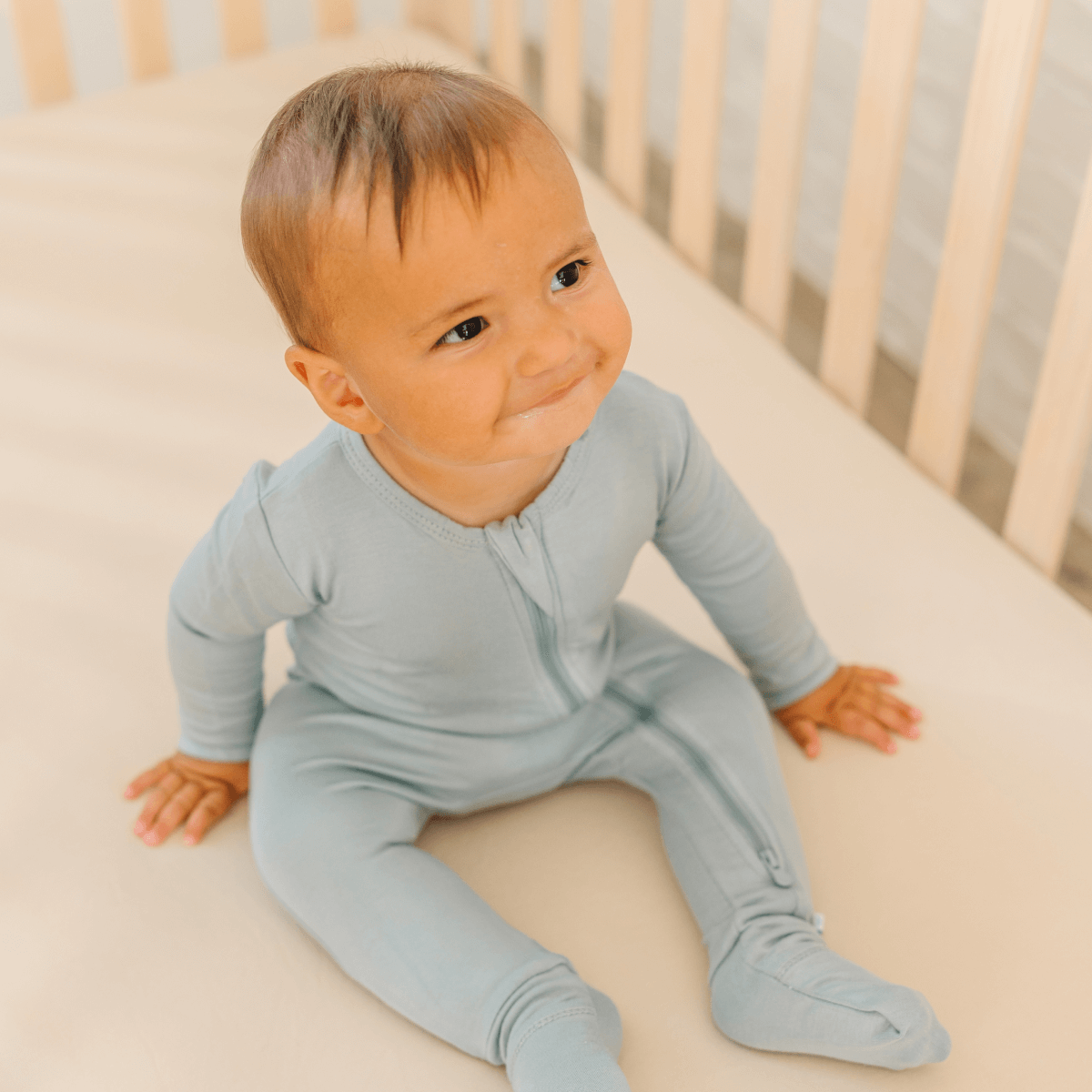 Baby in soft bamboo pajamas with DreamCuffs® from Dreamland Baby, featuring footed design and cozy cuffs for comfort.