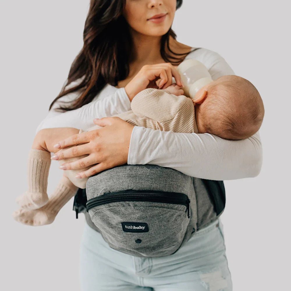 Baby wearing Tushbaby hip carrier with toddler seated comfortably, showcasing ergonomic design and secure straps.
