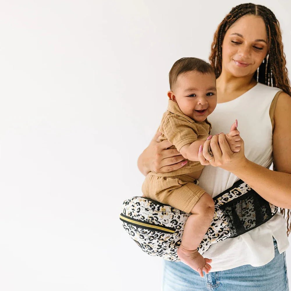 Tushbaby Hip Carrier for babies and toddlers, beige fabric with adjustable straps and ergonomic design for comfortable carrying.