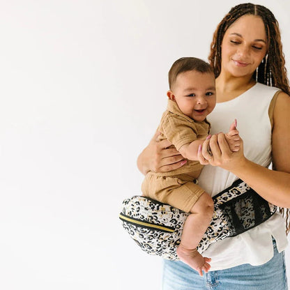 Tushbaby Hip Carrier for babies and toddlers, beige fabric with adjustable straps and ergonomic design for comfortable carrying.