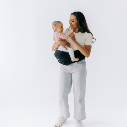 Tushbaby Hip Carrier for babies and toddlers, shown in a natural setting with a child securely seated in the ergonomic carrier.