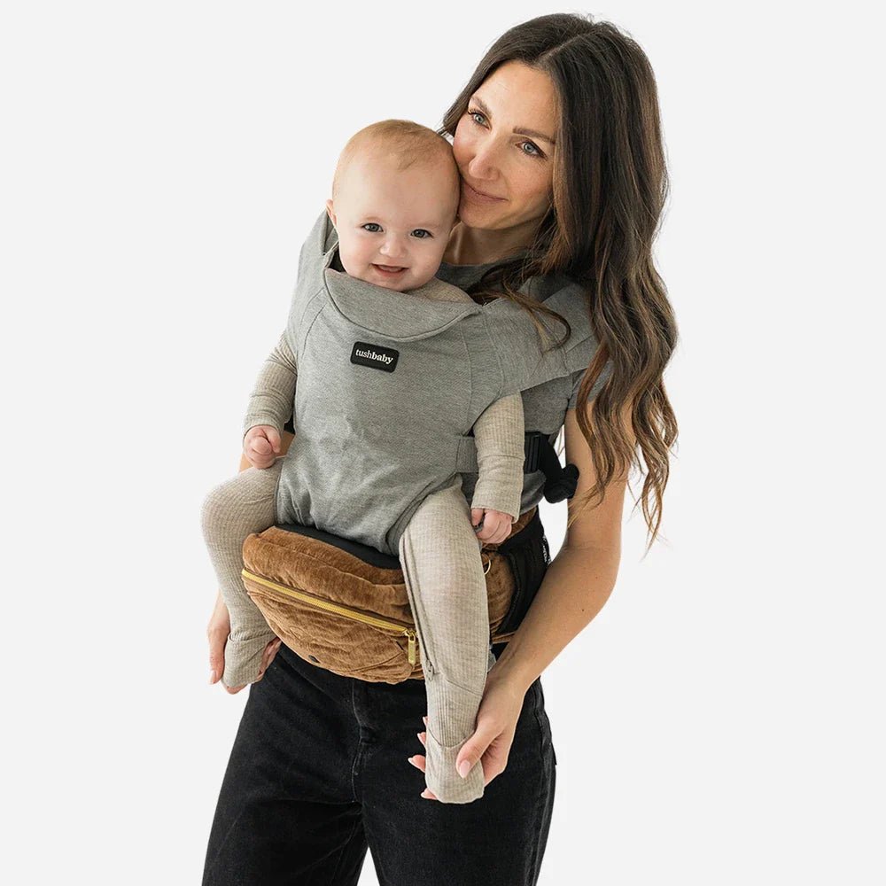 Baby wearing Tushbaby Hip Carrier, a comfortable toddler and baby hip carrier from Tushbaby, with supportive straps and ergonomic design.