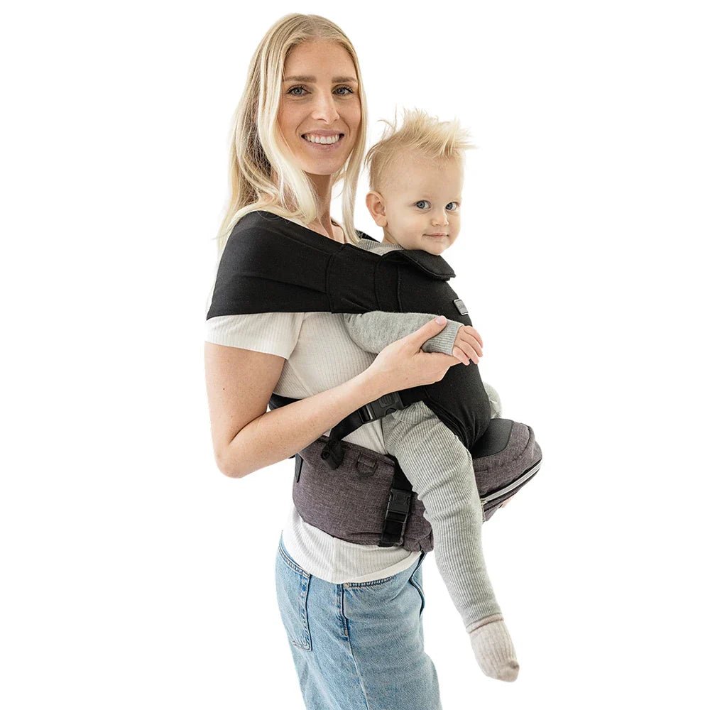 Baby sitting in the Tushbaby Hip Carrier, a supportive ergonomic carrier for toddlers by Tushbaby, shown in a neutral setting.
