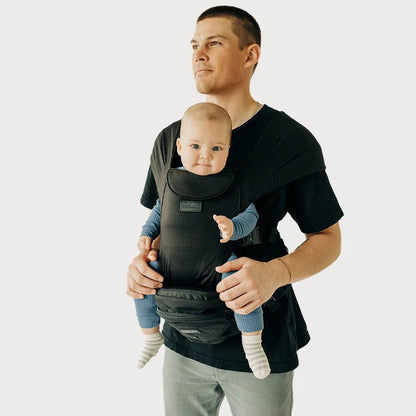 Tushbaby hip carrier for babies and toddlers, beige fabric with adjustable straps, worn around the waist for hands-free carrying.