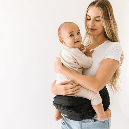 Baby wearing Tushbaby hip carrier on parent’s hip, showcasing ergonomic design for comfortable baby and toddler carrying.
