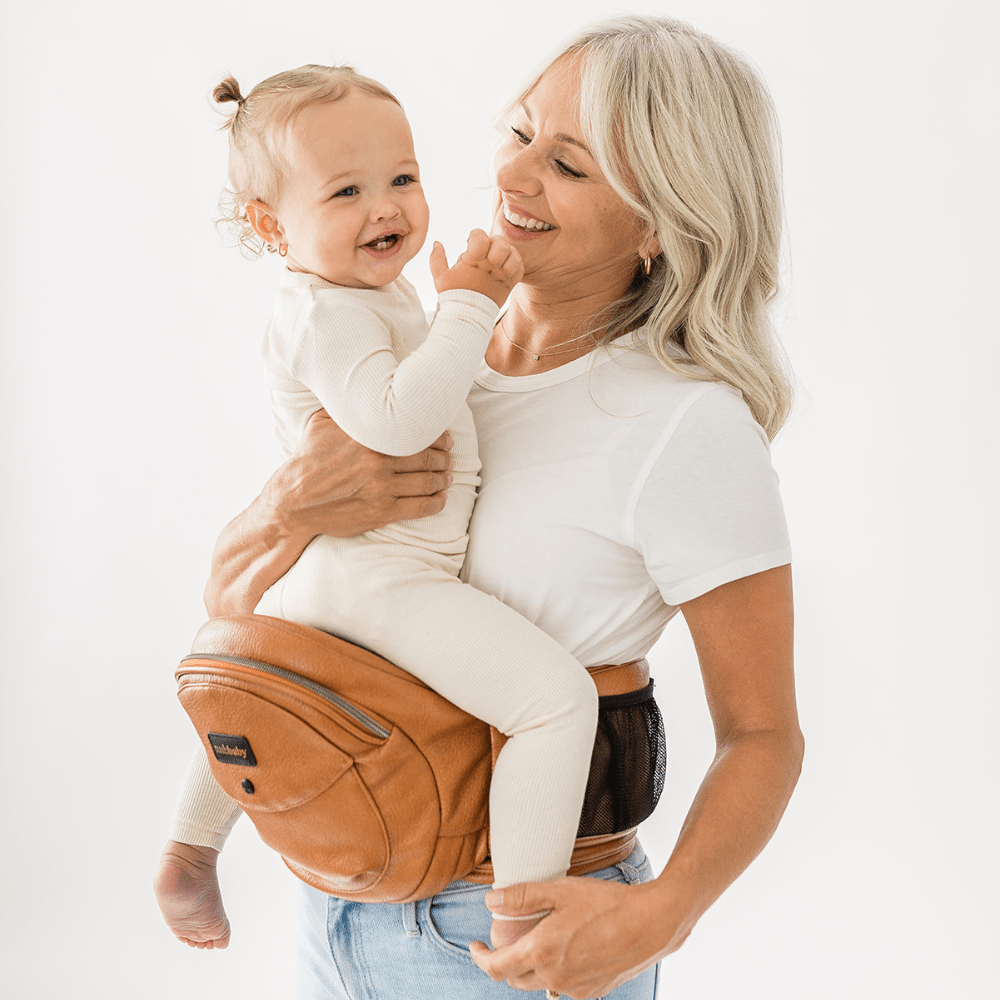 Tushbaby Hip Carrier for babies and toddlers, beige fabric with adjustable straps and ergonomic design for comfortable carrying.