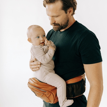 Tushbaby Hip Carrier for babies and toddlers, beige fabric with adjustable straps, designed for comfortable carrying.