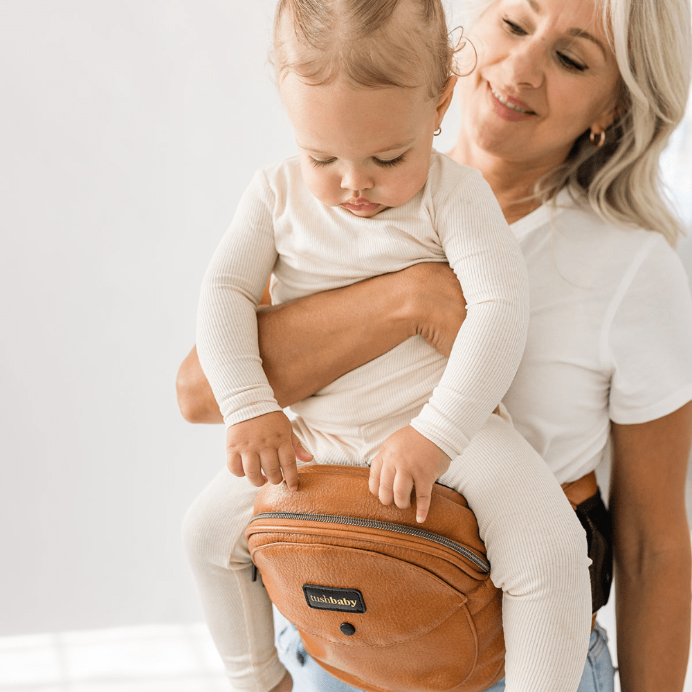 Tushbaby Hip Carrier for baby and toddler, featuring adjustable straps and padded support in a neutral color.
