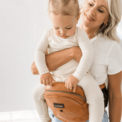 Tushbaby Hip Carrier for baby and toddler, featuring adjustable straps and padded support in a neutral color.